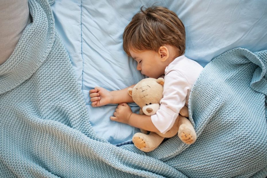 Un bambino che dorme con un peluche sul suo letto